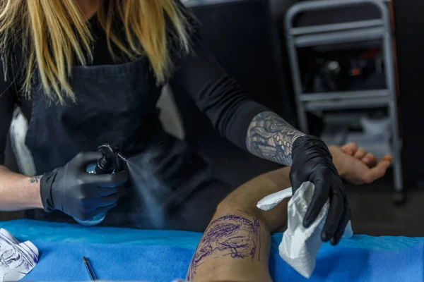 A tattoo artist woman with a spray on the arm of a client — Stock Photo, Image