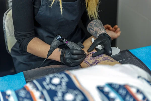 Une femme tatoueuse dessine avec la machine à tatouer, le contour de — Photo