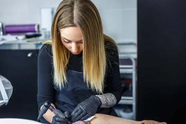 Blonde artist draws a tattoo with maximum concentration