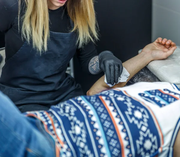 A tattooist woman cleans the skin of the arm of the person who i