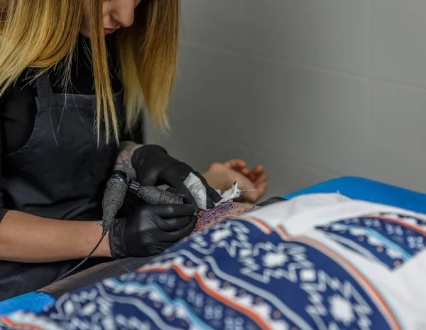 Ein tätowierter Künstler mädchen zeichnet sorgfältig ein tätowierung mit ihrem tätowierer ma — Stockfoto