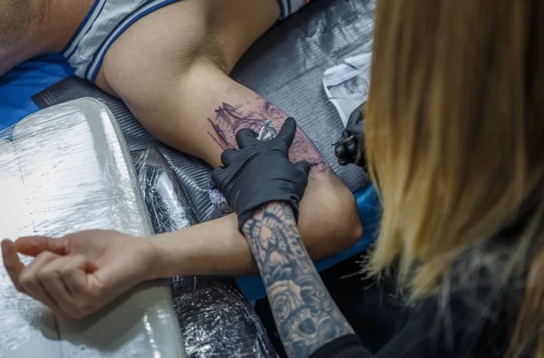 A tattooist woman is painting a tattoo on the arm of a client — Stock Photo, Image