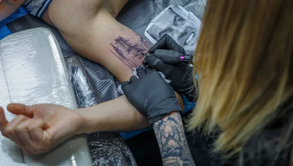 A tattooist blonde girl is depicting a tattoo on the arm of a cl — Stock Photo, Image