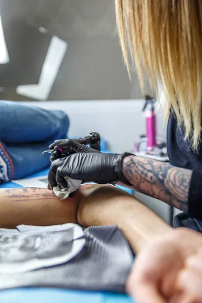 A tattoo artist woman sketches with her needle in the arm of a man — Stock Photo, Image