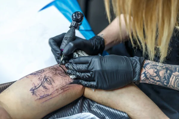 A tattoo artist woman is sketching with her needle in the arm of a man — Stock Photo, Image