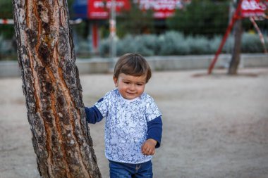 Güzel bir çocuk yanında bir ağaç büyük bir parkta oynarken gülümsedi