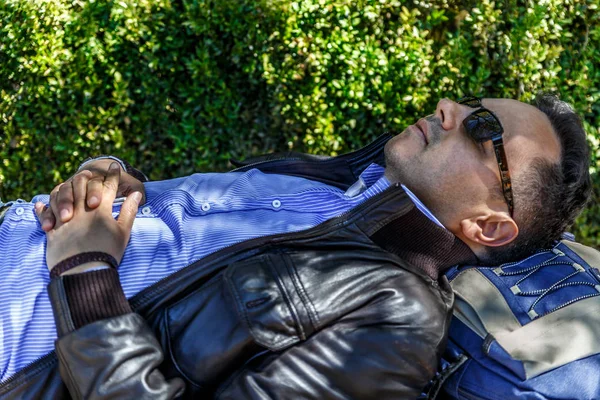 Чоловік у шкіряній куртці та чорних окулярах, відпочиває на лавці — стокове фото