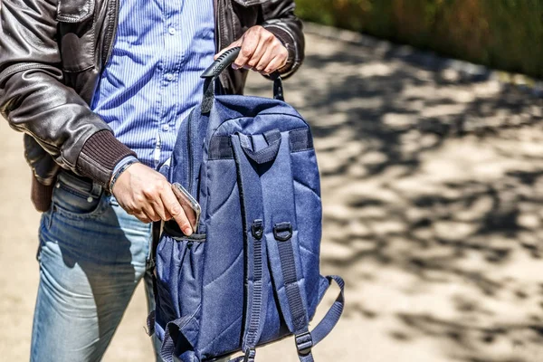 Um homem guarda o telemóvel na mochila azul. — Fotografia de Stock