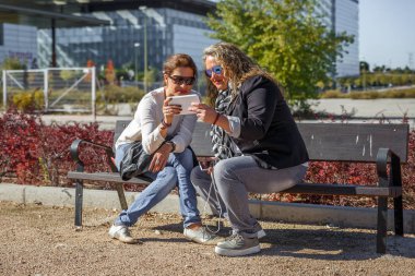 İki kadın bir tablet gözden geçirirken gülümseme bankta oturan