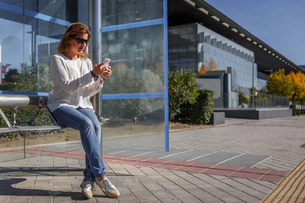 Rahat kıyafetler ile ince kadın dikkatle onu mobil pho inceliyor