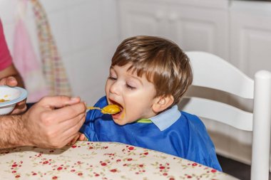 Sevimli bir küçük sarışın çocuk çok arzu ile havuç püresi yiyor