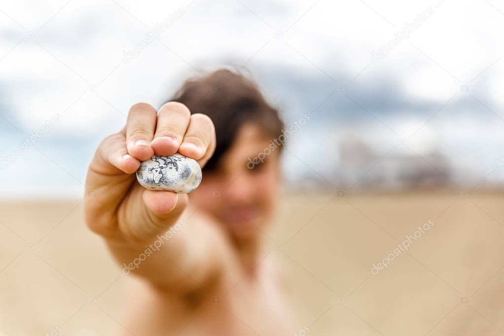 A boy teaches a small white stone on a quiet beach