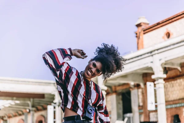 Genç, afro tarzı bir turist kadın şehirde yürürken kameraya gülümsüyor. — Stok fotoğraf