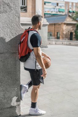Bir atlet basketbolcunun arka planı, büyük bir sütuna yaslanmış, bir sonraki maçını düşünürken