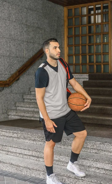 Strong basketball player leaves the portal of a large building with a basketball and a backpack — Stock Photo, Image