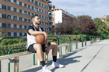 Şehir sahasında oturan güçlü bir basketbolcu, top ile oyun oynamak için bekliyor.