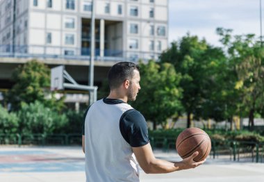 Sporcu, güneşli bir günde açık havada basketbol oynar.