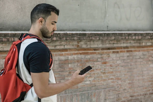 Sporcu bir akıllı telefonu kontrol ederken rahatça bir duvarın yanında yürüyor.