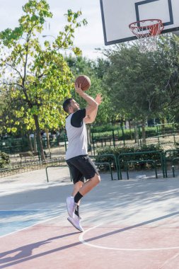 Bir şehir basketbolcusu basketbol sahasında topuyla atış yapar.