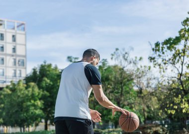 Güçlü oyuncu, güneşli bir öğleden sonra açık havada basketbol topunu toplar.