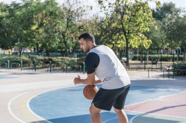 Şehrin ortasında bir sahada basketbol oynayan genç bir adam.