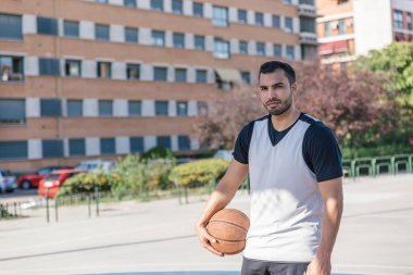 Çekici basketbolcu, topuyla şehir sahasında poz verirken gülümseyen kameraya bakar.