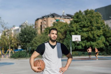 Güçlü vücut basketbolcusu, şehir sahasında basketbol topuyla kameranın önünde meydan okuyor.