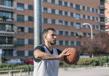 Güçlü bir atlet basketbolcu topuyla metal bir sütuna yaslanıyor.