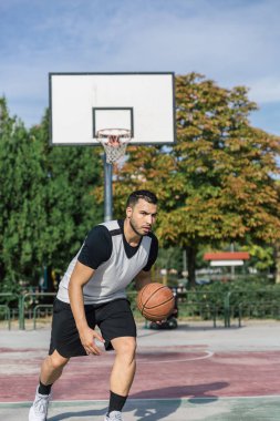 Şehir sporcusu dışarıda basketbol antrenmanı yapıyor. Sol koluyla top oynuyor.