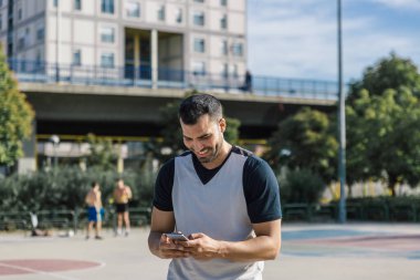 Çekici, gülümseyen bir sporcu spor sahasının ortasında akıllı telefonuyla bir mesaj yazar.