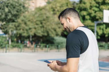 Güçlü bir atlet cep telefonunu dışarıda basketbol sahasının ortasında kontrol eder.