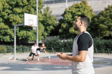 Elinde cep telefonu tutarken gülümseyen bir erkek sporcunun yan görüntüsü
