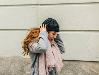 Genç sarışın kız, bir şehrin caddesinde yürürken yün bir şapka takıyor.