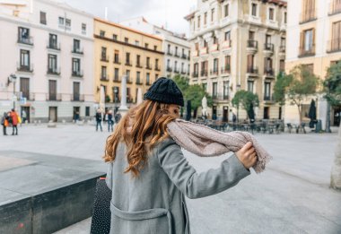 Sırtı büyük pembe eşarbını sallayan sarışın kız alışveriş torbalarıyla şehirde yürürken...