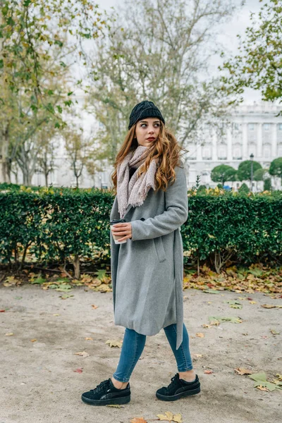 Une jeune femme européenne se promène dans un parc avec des vêtements chauds tout en prenant un café à emporter — Photo
