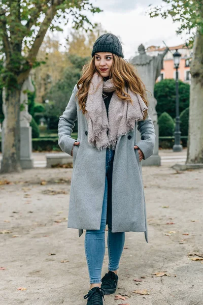 Jeune femme blonde européenne, porte ses mains dans les poches de son manteau, tout en marchant dans un parc par une journée froide — Photo