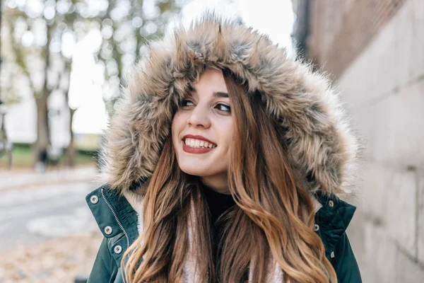 Blanc blond fille avec manteau et un grand capuchon sourit à la caméra par une journée froide — Photo