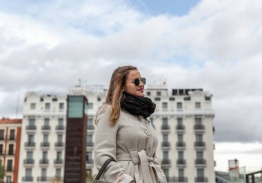 Beyaz önlüklü, siyah eşarplı çekici beyaz kadın şehirde gülümsüyor.