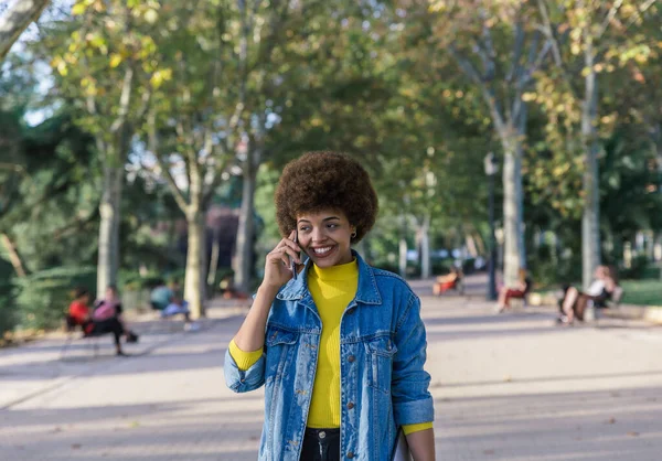 Beautiful brunette girl with afro hair smiles with her perfect white teeth while talking on her mobile phone — Stock Photo, Image
