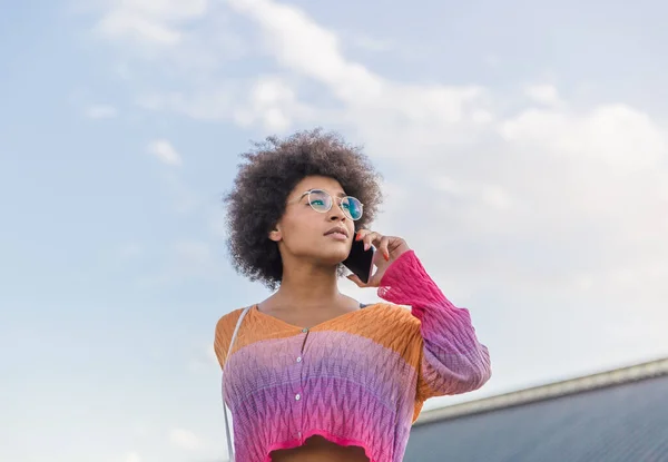 Beautiful intellectual style afro haired girl talks to her mobile phone representing freedom on a clear spring day