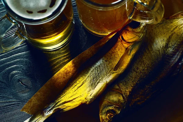 Glas med öl och fisk på ett mörka träbord. — Stockfoto