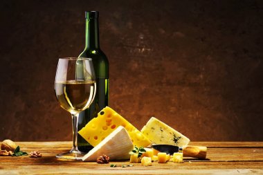 Peynir ve bir şişe şarap ahşap bir masa üzerinde bir cam ile.