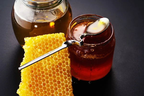 Honing in glazen potten en honingraat op een zwarte achtergrond. — Stockfoto