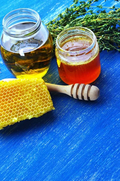 Honey in glass jars and honeycomb on a blue old board. — Stock Photo, Image