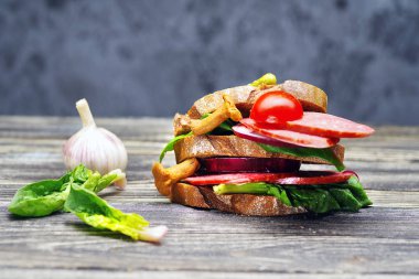 Büyük taze sandviç salam ve koyu ahşap bir masa üzerinde sebze ile.