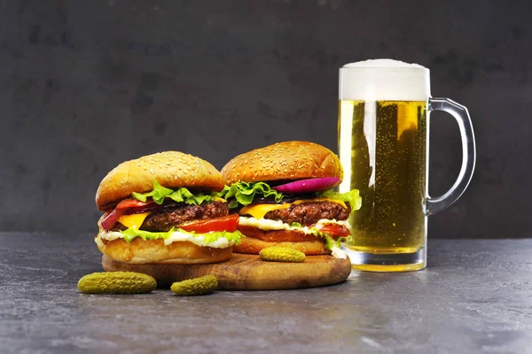 Dos deliciosas hamburguesas con un vaso de cerveza sobre un fondo gris . — Foto de Stock