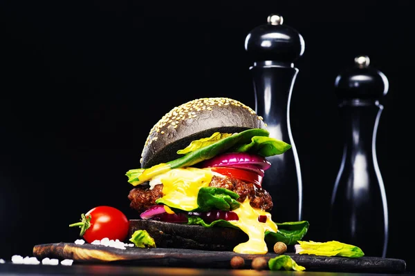 Czarny burgera z przyprawami na czarnym tle. — Zdjęcie stockowe