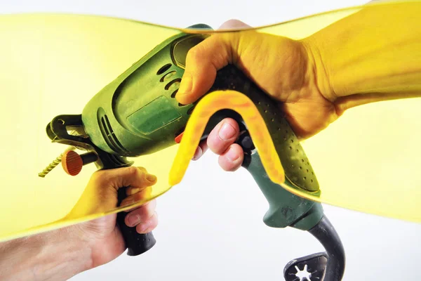 Vy över mäns händerna med en elektrisk borr genom gula skyddsglasögon. Första person vy. — Stockfoto
