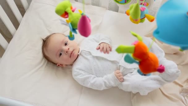 Hermoso bebé de 3 meses de edad acostado en la cama y mirando colorido móvil giratorio — Vídeos de Stock