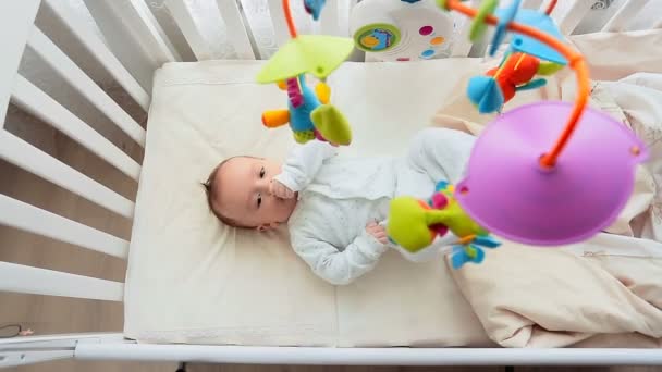 Vue de dessus plan de bébé mignon avec sucette couché dans la crèche et regardant filer mobile — Video